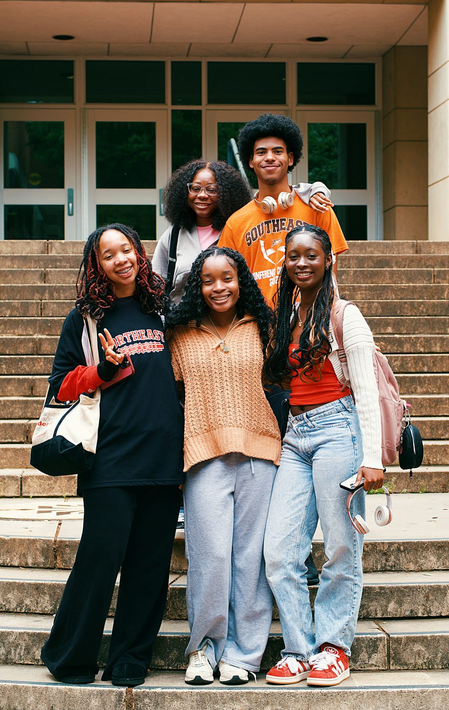 Four smiling students standing together on university steps